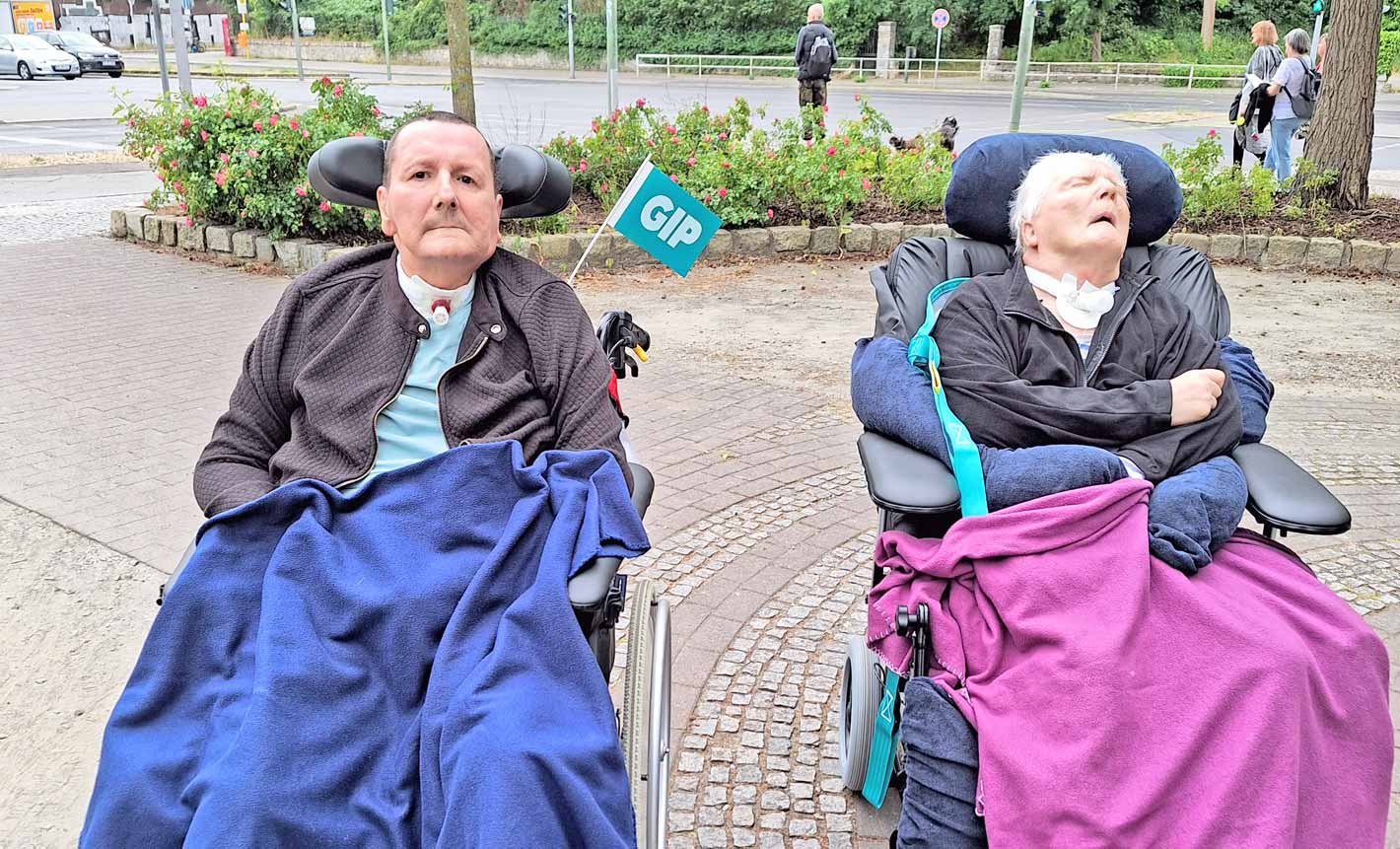 Zwei pflegebedürftige Menschen im Rollstuhl unterwegs.